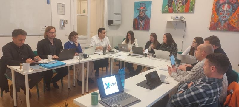 Panorama of the partners around the table, with the X-VET logo on a laptop