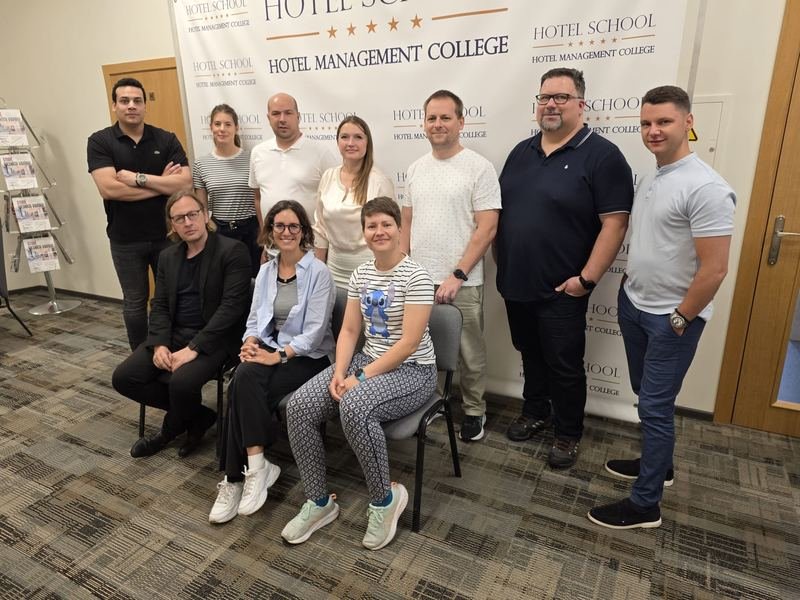 The partners in front of the HOTEL SCHOOL banner